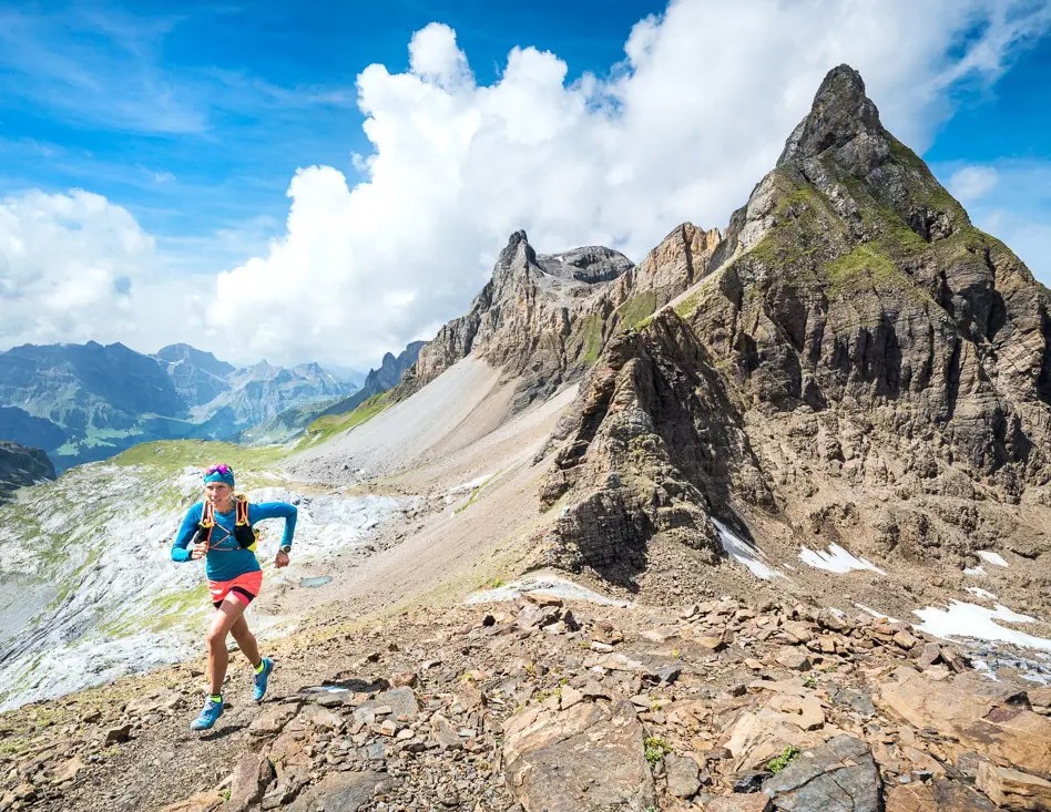 Photo d'une femme qui court sur une crête rocheuse, des montagnes en arrière plan